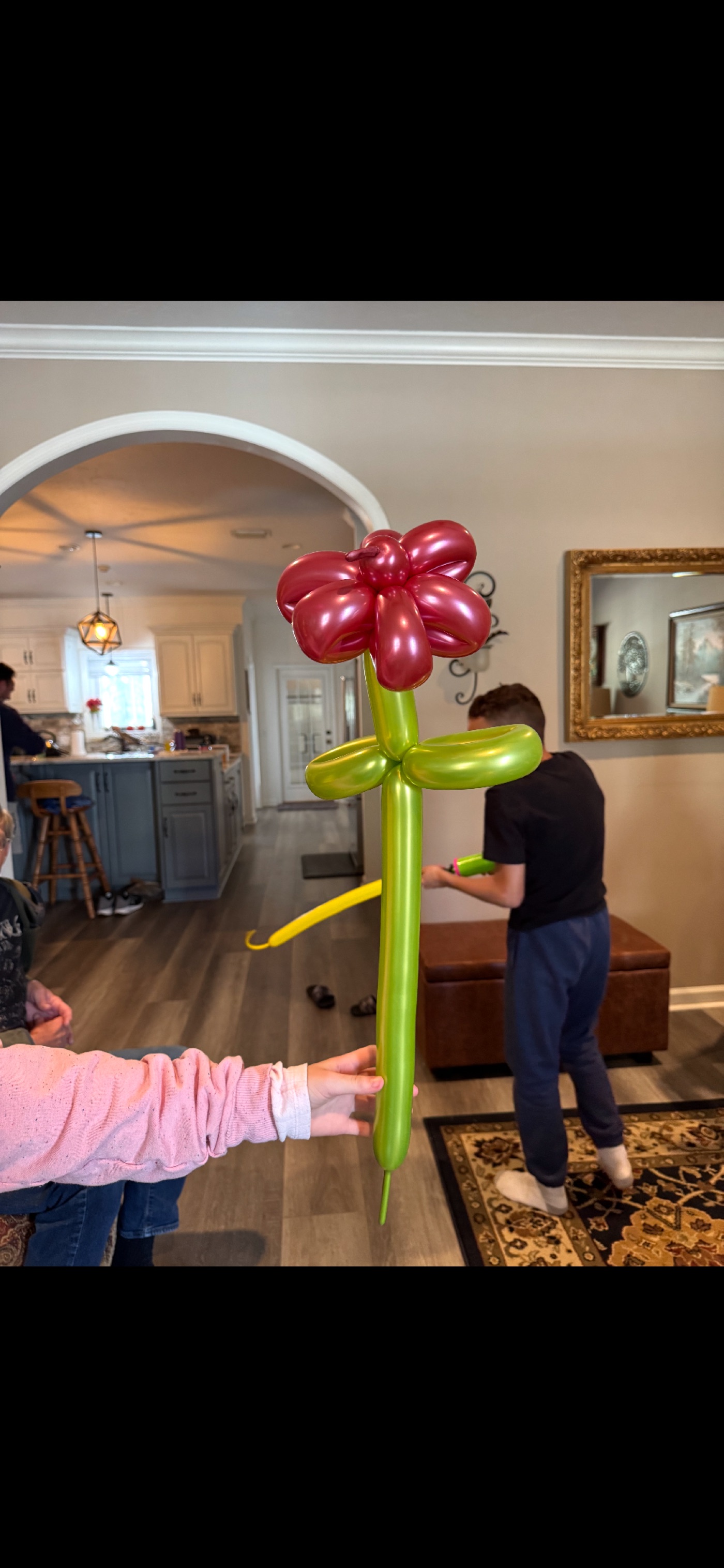 A red and green balloon flower held up at a family gathering.